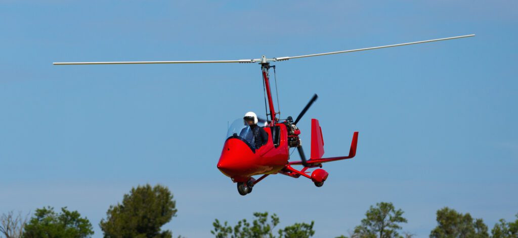 A red gyrocopter flying in the blue sky.