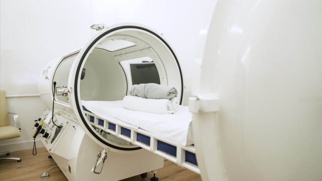 A modern hyperbaric oxygen therapy chamber with a neatly prepared bed inside.