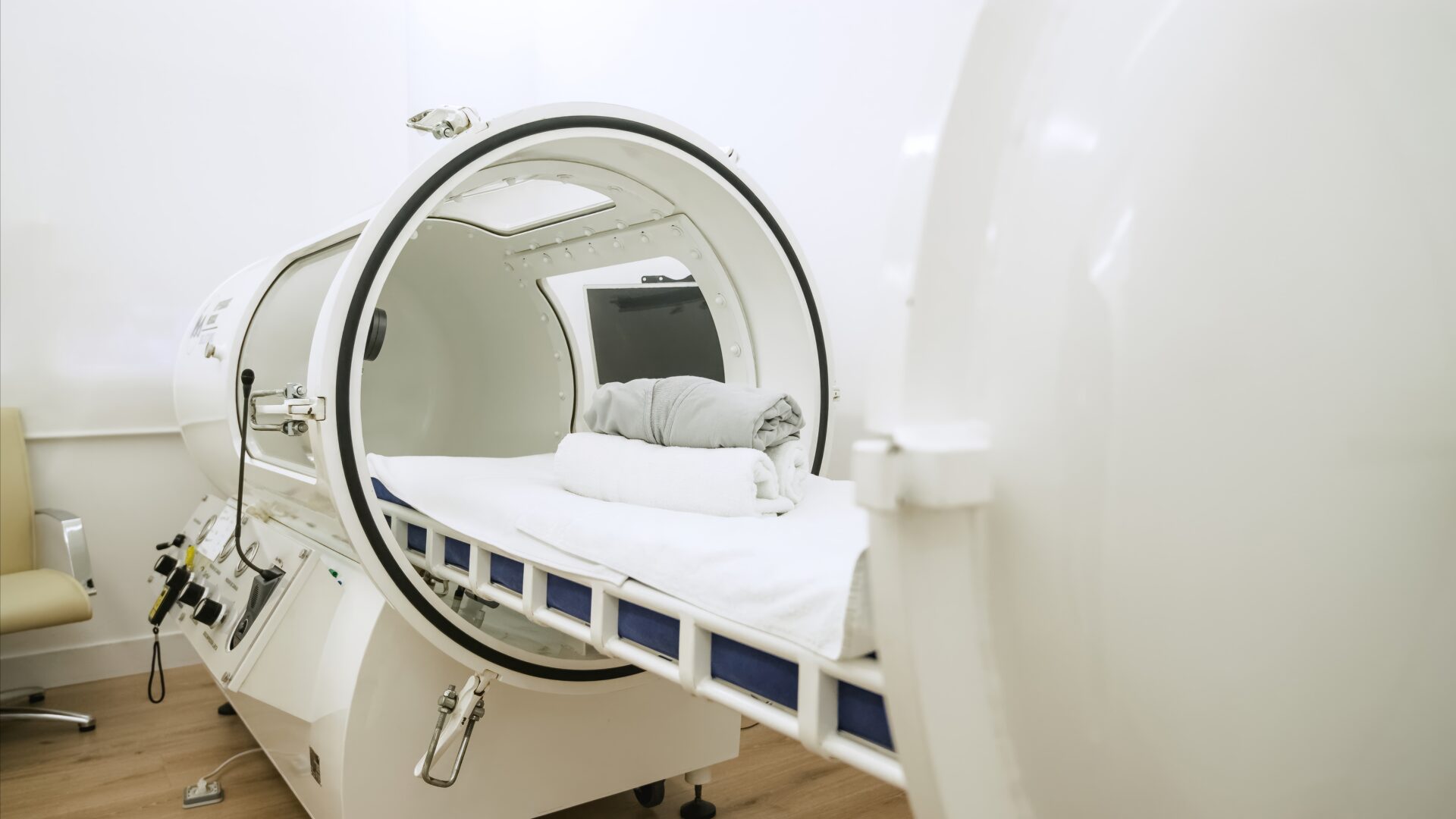 A modern hyperbaric oxygen therapy chamber with a neatly prepared bed inside.