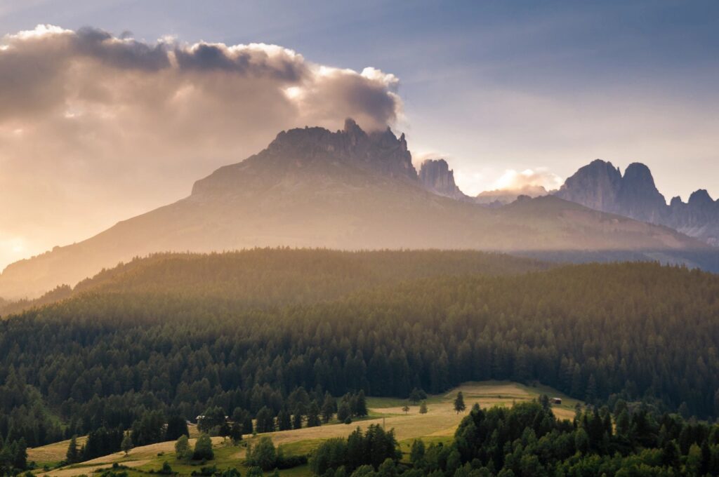 Majestic mountain peak with clouds and mist over a lush forest and fields.