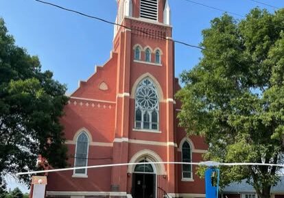 A tall red brick church tower with a clock and arched windows.