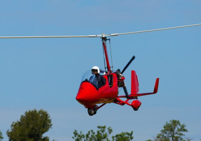 A red gyrocopter flying in the blue sky.