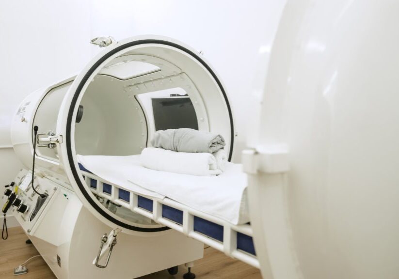 A modern hyperbaric oxygen therapy chamber with a neatly prepared bed inside.